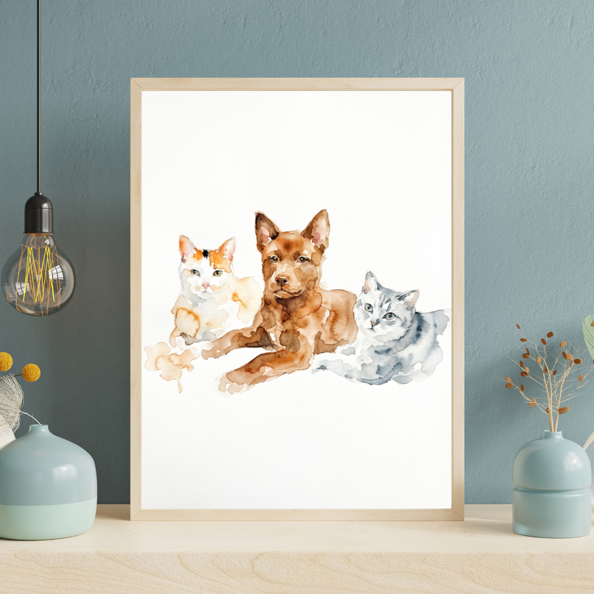 Framed watercolor portrait of a brown dog sitting between two cats, displayed on a wooden shelf in a cozy room.