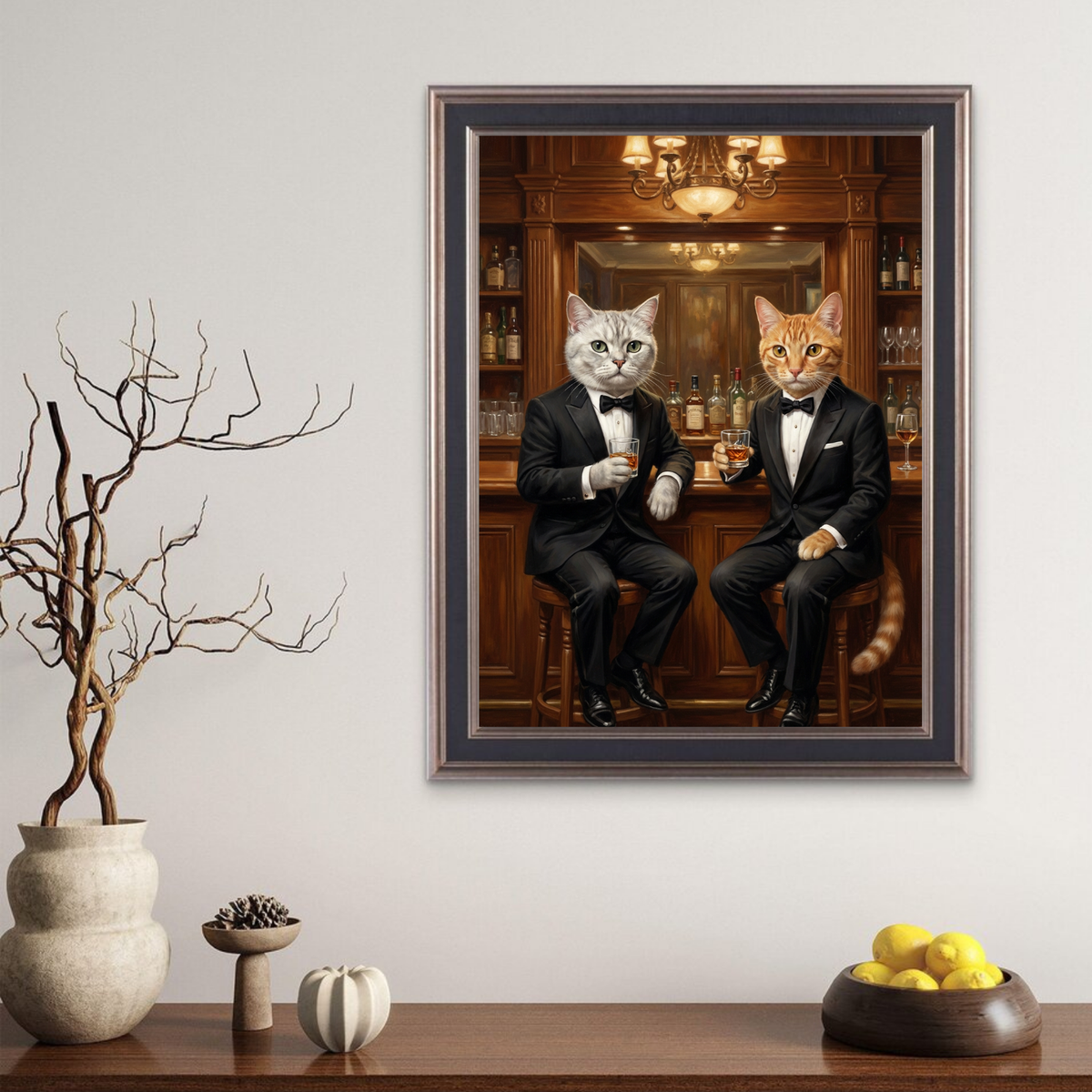 A framed oil-style portrait of a grey and an orange cat dressed in tuxedos, drinking whiskey at a wood-paneled bar.
