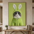 A framed, realistic portrait of a gray and white cat wearing a fuzzy mint-green bunny hoodie against a solid green