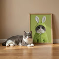 A framed custom portrait of a cat in a fuzzy green bunny-ear hoodie, displayed on a wooden floor next to